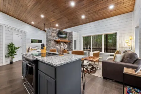 This open-concept living space is basically the heart of everything—an airy, light-filled zone where you can cook, gather around the fireplace, watch the forest through those massive windows, and feel like you've got your own private retreat all figured o