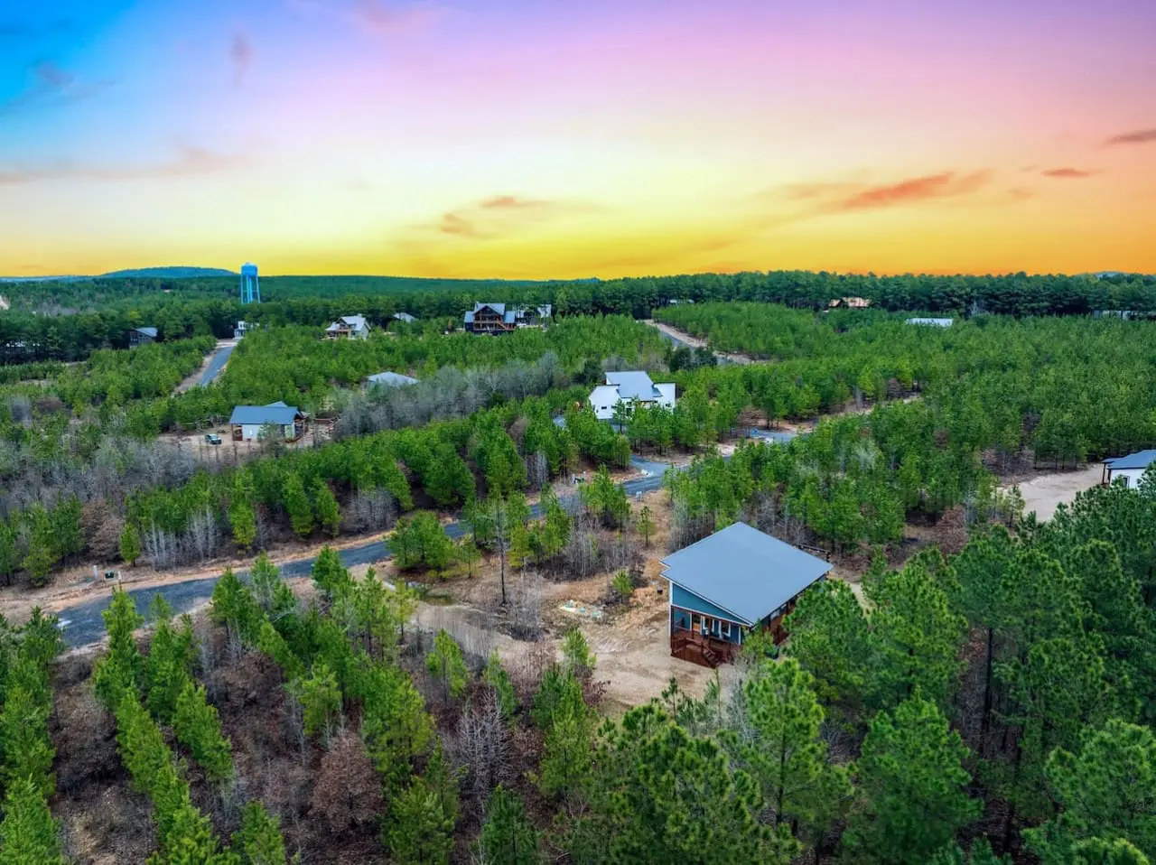 From up here, you can see your whole private world—tree-lined roads, scattered cabins, that blue water tower in the distance—and somehow it all feels like it belongs to you.