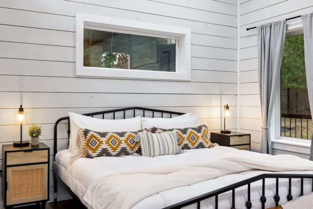 Wake up to forest views framed by that perfect horizontal window, snuggle under those mustard and charcoal patterned blankets, and realize this bedroom is basically the cozy, modern cabin aesthetic you've been dreaming about.