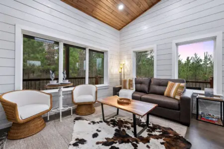 This sunroom is basically a treehouse for adults—wrap yourself in those cozy chairs, watch the forest come alive through every window, and pretend your real life doesn't exist for a weekend.