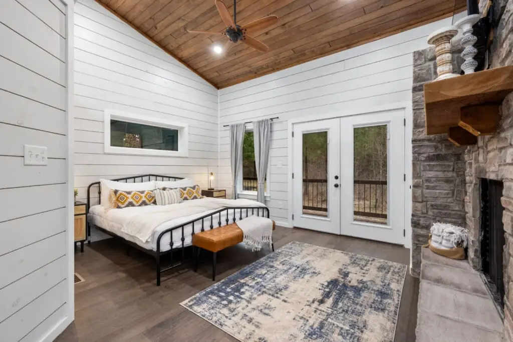 Wake up in this bedroom and you've got everything—a cozy metal bed, those stone fireplace vibes, and French doors that open straight onto your private forest view.
