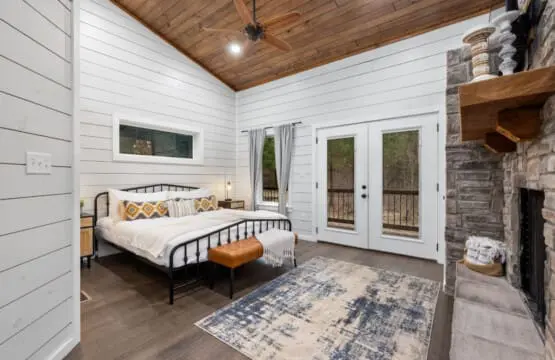 Wake up in this bedroom and you've got everything—a cozy metal bed, those stone fireplace vibes, and French doors that open straight onto your private forest view.