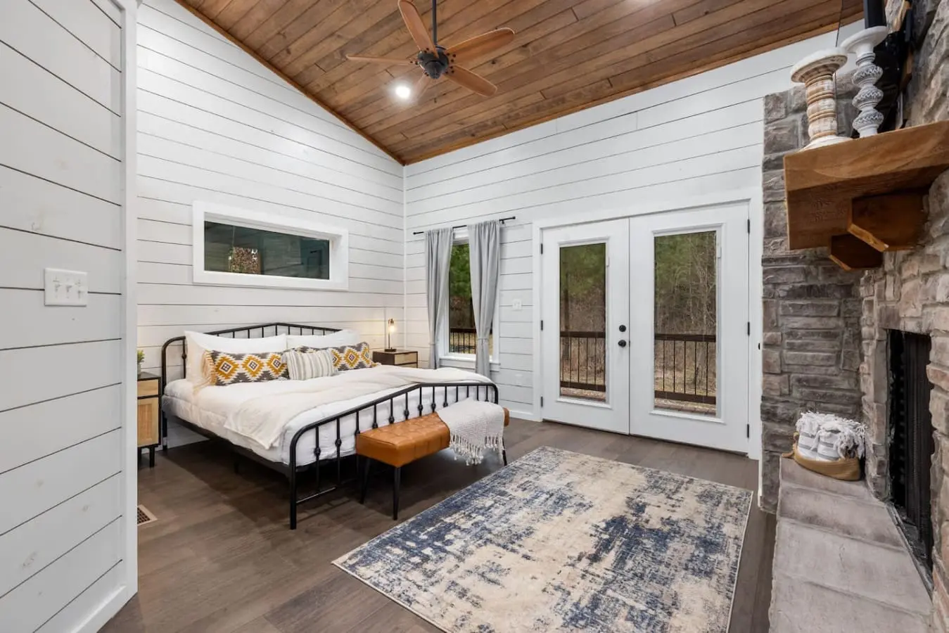 Wake up in this bedroom and you've got everything—a cozy metal bed, those stone fireplace vibes, and French doors that open straight onto your private forest view.