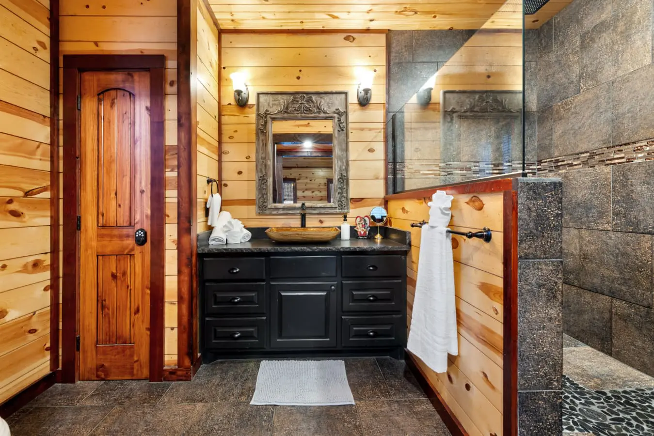 The bathroom features rustic pine wood walls and a dark, multi-drawer vanity with a bowl-style sink.