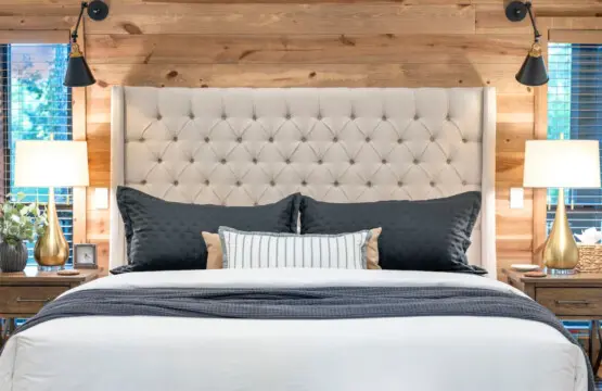 This bedroom is basically a five-star hotel moment with that perfectly tufted headboard, moody black bedding, those swing-arm reading lights, and windows that frame the treetops like living artwork.