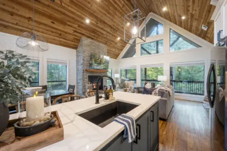 This open-concept kitchen-to-living-room flow with those soaring wood ceilings, endless windows framing the forest, and a fireplace that's basically begging you to settle in is exactly the kind of space where you'd want to spend literally all your time.