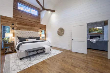 This master bedroom with that soaring vaulted ceiling, the cozy wood accent wall, and those skylights flooding in natural light basically feels like sleeping inside a treehouse designed by someone with seriously good taste.