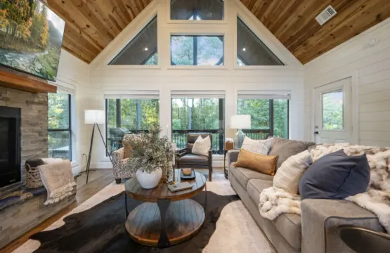 This living room basically feels like someone built the ultimate forest hideaway where you can sink into a cozy sofa, stare out at endless trees through those massive windows, and forget that the outside world even exists.