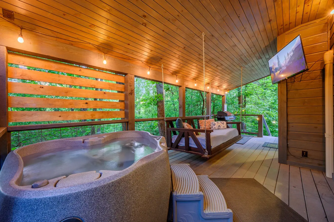 The outdoor living space includes a private hot tub, a wooden hanging daybed, and a wall-mounted television.