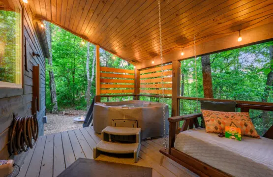 Spacious deck featuring a relaxing hot tub and cozy swing couch, perfect for unwinding while enjoying the peaceful outdoor views