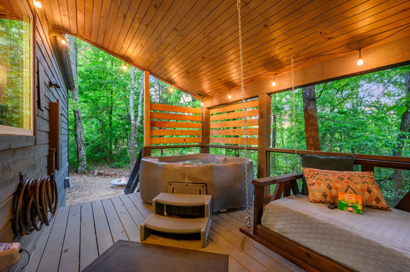 Spacious deck featuring a relaxing hot tub and cozy swing couch, perfect for unwinding while enjoying the peaceful outdoor views