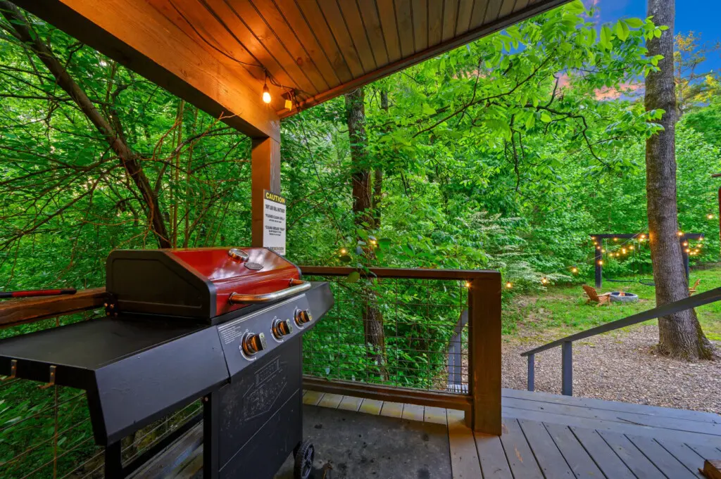 The deck is equipped with a gas grill for cooking and overlooks a rustic backyard with a fire pit area.