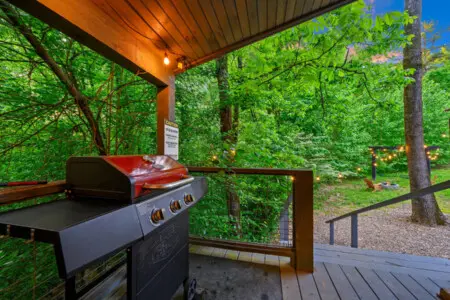 The deck is equipped with a gas grill for cooking and overlooks a rustic backyard with a fire pit area.