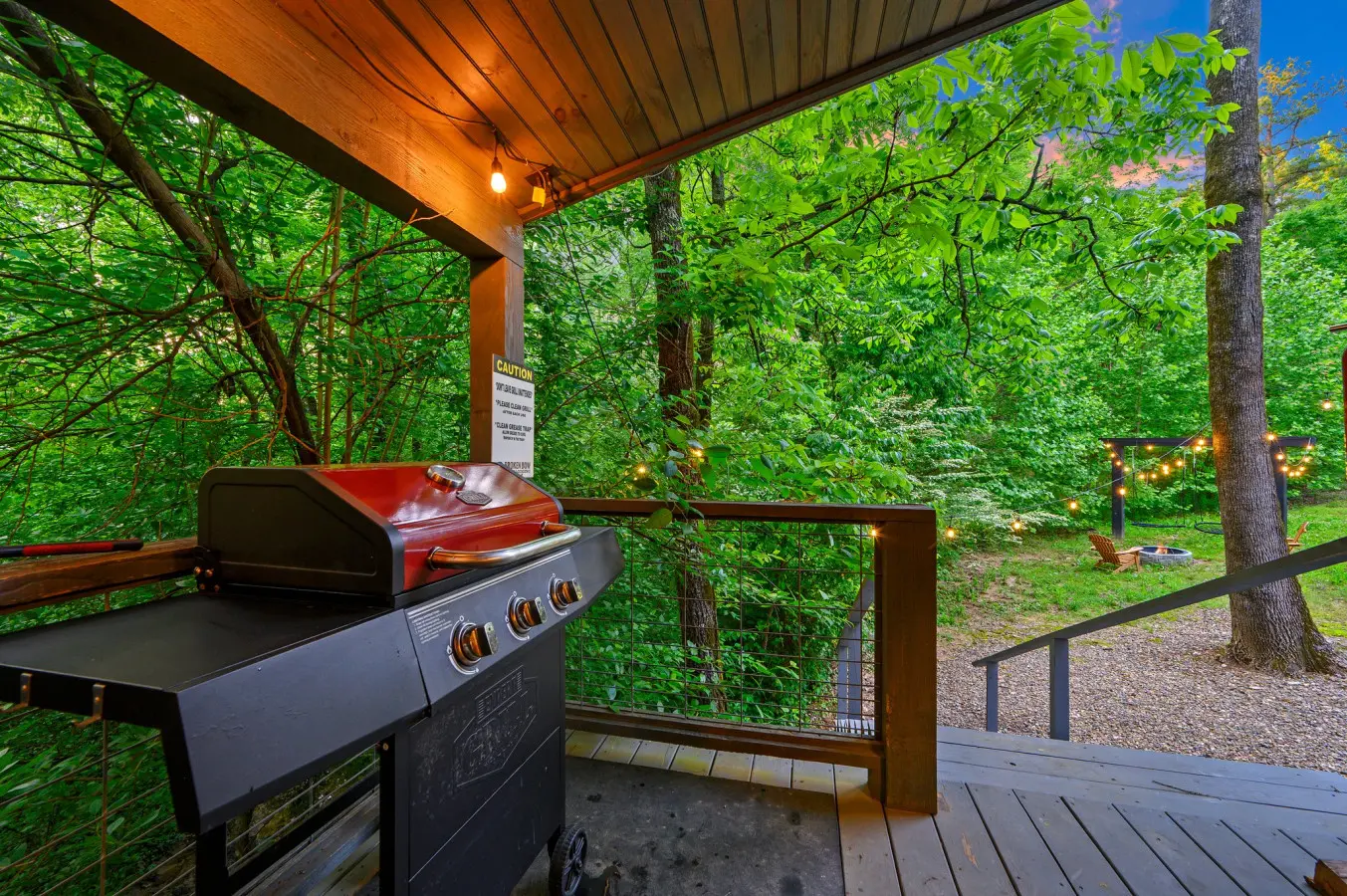 The deck is equipped with a gas grill for cooking and overlooks a rustic backyard with a fire pit area.