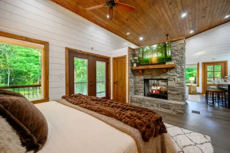 This bedroom's basically a forest viewing platform that happens to have a really comfortable bed—those glass doors, the fireplace, the whole vibe just says "your alarm clock can wait."
