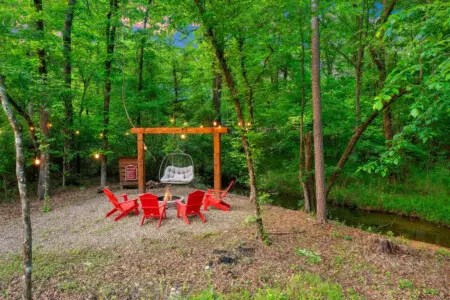 Gather around this fire pit with those bold red Adirondack chairs, string lights glowing overhead, and the forest wrapped around you like a blanket—this is the kind of setup that turns a random Tuesday night into the memory everyone's still talking about