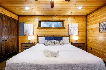 This cozy log cabin bedroom feels like a mountain retreat with its warm wood walls, modern amenities, and that perfect window view.