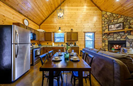 This open-concept cabin feels perfect for gathering with its wood ceilings, stone fireplace, and modern kitchen all in one cozy space.
