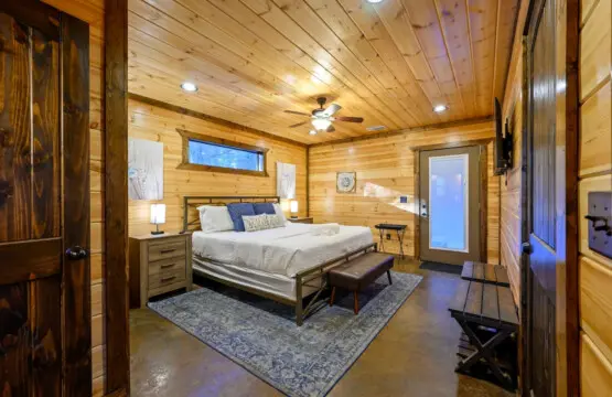 This spacious master bedroom features warm wood throughout, a cozy bed, and direct access to the outdoors.