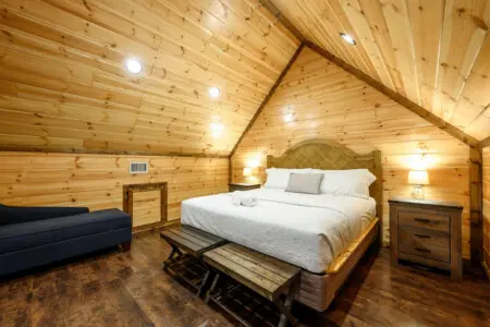 This cozy A-frame cabin bedroom features vaulted wood ceilings, a comfortable king bed, and warm ambient lighting.