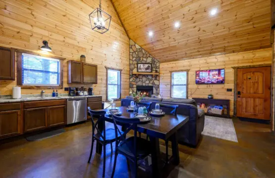 This open-concept cabin features a gorgeous wood-beamed ceiling, stone fireplace, and modern kitchen all in one stunning living space.