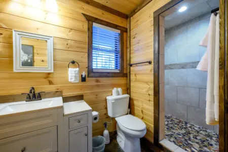 This cozy cabin bathroom features warm wood walls, a clean white vanity, and a spacious walk-in shower with tile accents.