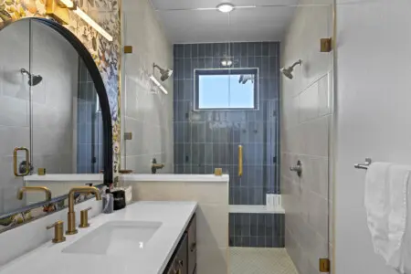 This bathroom has that dual showerhead setup with blue accent tile and brass hardware that feels like a boutique hotel.