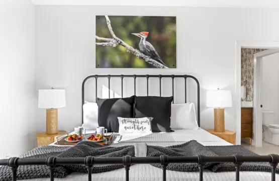 The primary bedroom features a striking wrought iron bed with crisp linens and a beautiful woodpecker photograph above.