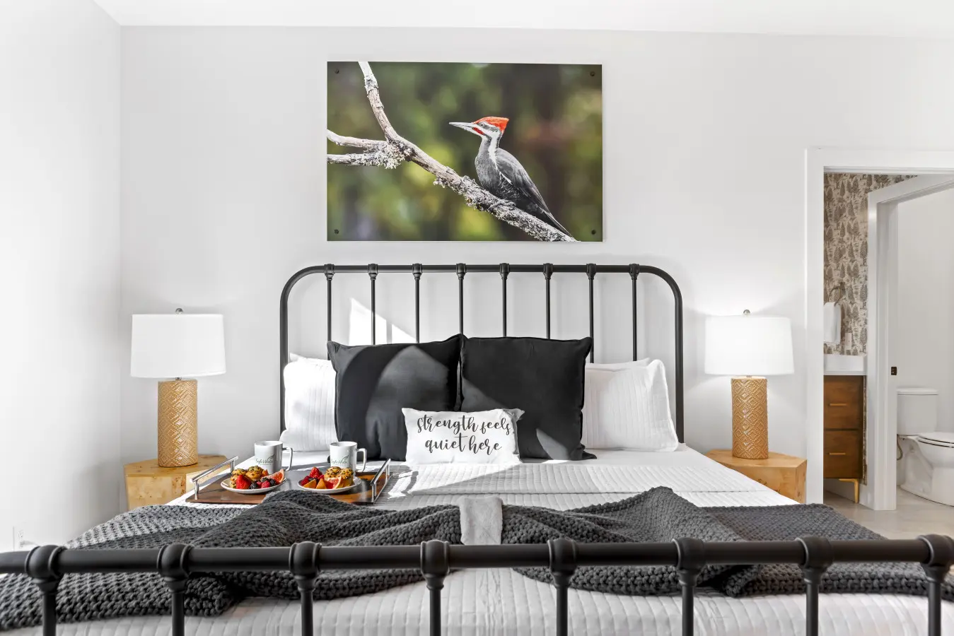 The primary bedroom features a striking wrought iron bed with crisp linens and a beautiful woodpecker photograph above.