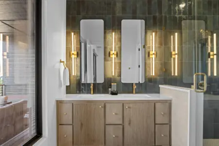 The double vanity has those moody green tiles and brass sconces that make getting ready feel a little more elevated.
