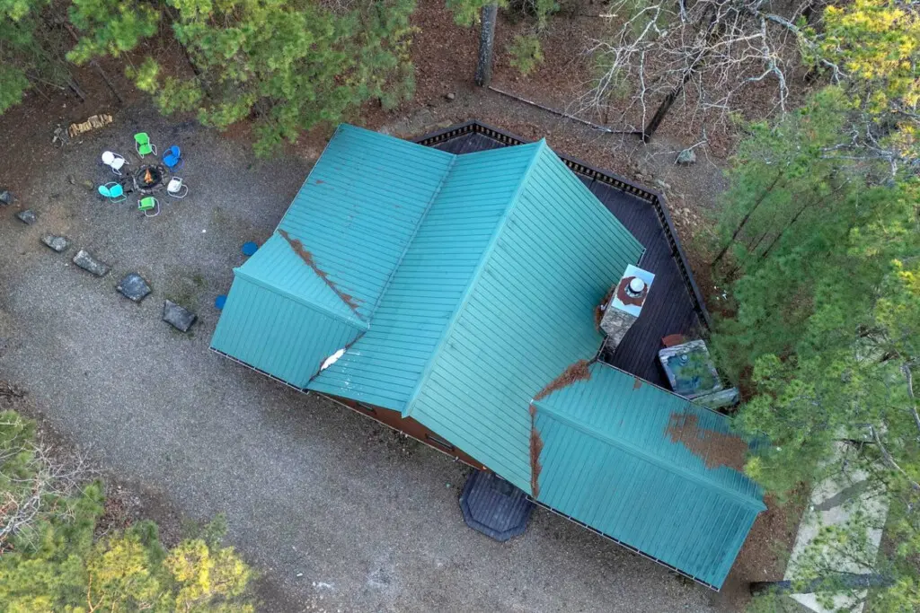 Cozy forest cabin with a stunning turquoise metal roof, perfect for an intimate woodland retreat surrounded by towering pines.