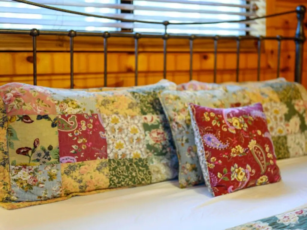 Cozy bedroom with a gorgeous wrought iron headboard and patchwork floral pillows that'll make you never want to leave.