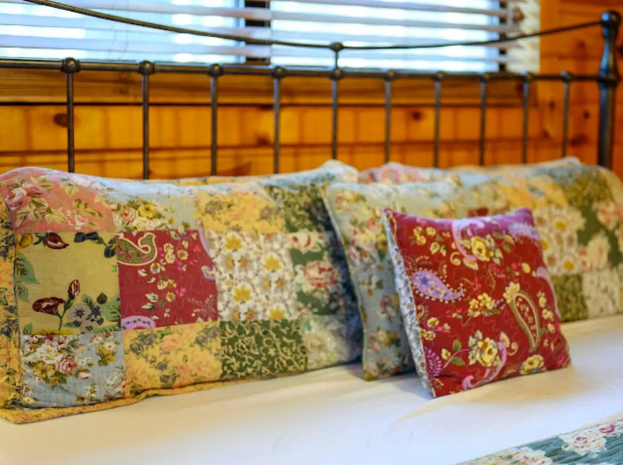 Cozy bedroom with a gorgeous wrought iron headboard and patchwork floral pillows that'll make you never want to leave.