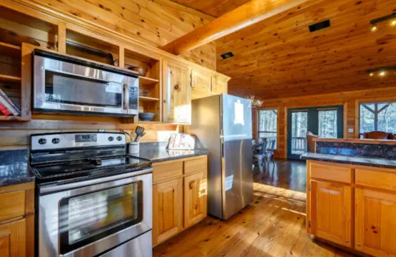 This gorgeous log cabin kitchen features stainless steel appliances, wood cabinetry, and amazing views of the forest.
