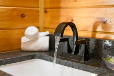 Water flows from a sleek black faucet into a pristine white sink set against warm wooden walls.