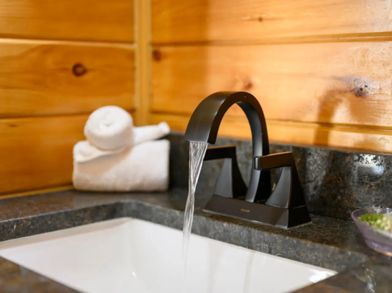Water flows from a sleek black faucet into a pristine white sink set against warm wooden walls.