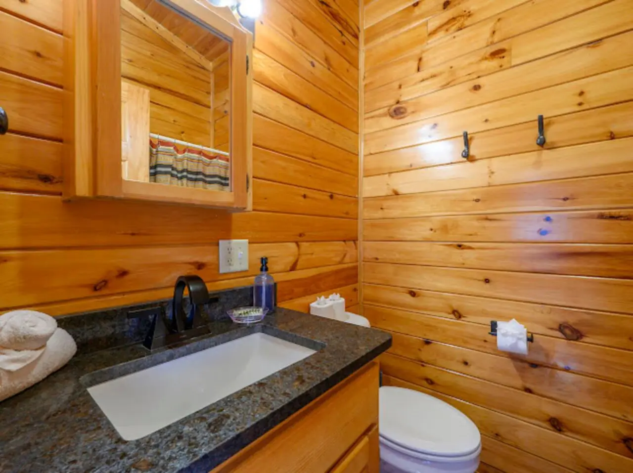 This cozy log cabin bathroom features rustic wood walls, granite countertops, and all the essentials for a comfortable stay.