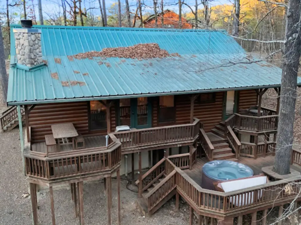 This gorgeous log cabin features wraparound decks, a hot tub, and a turquoise metal roof nestled in the woods.