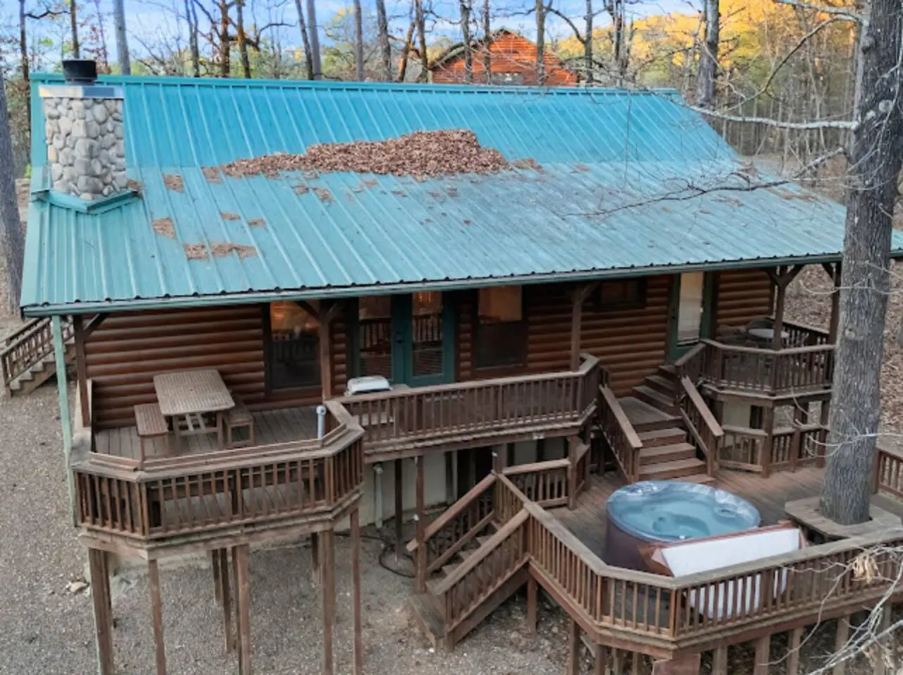 This gorgeous log cabin features wraparound decks, a hot tub, and a turquoise metal roof nestled in the woods.