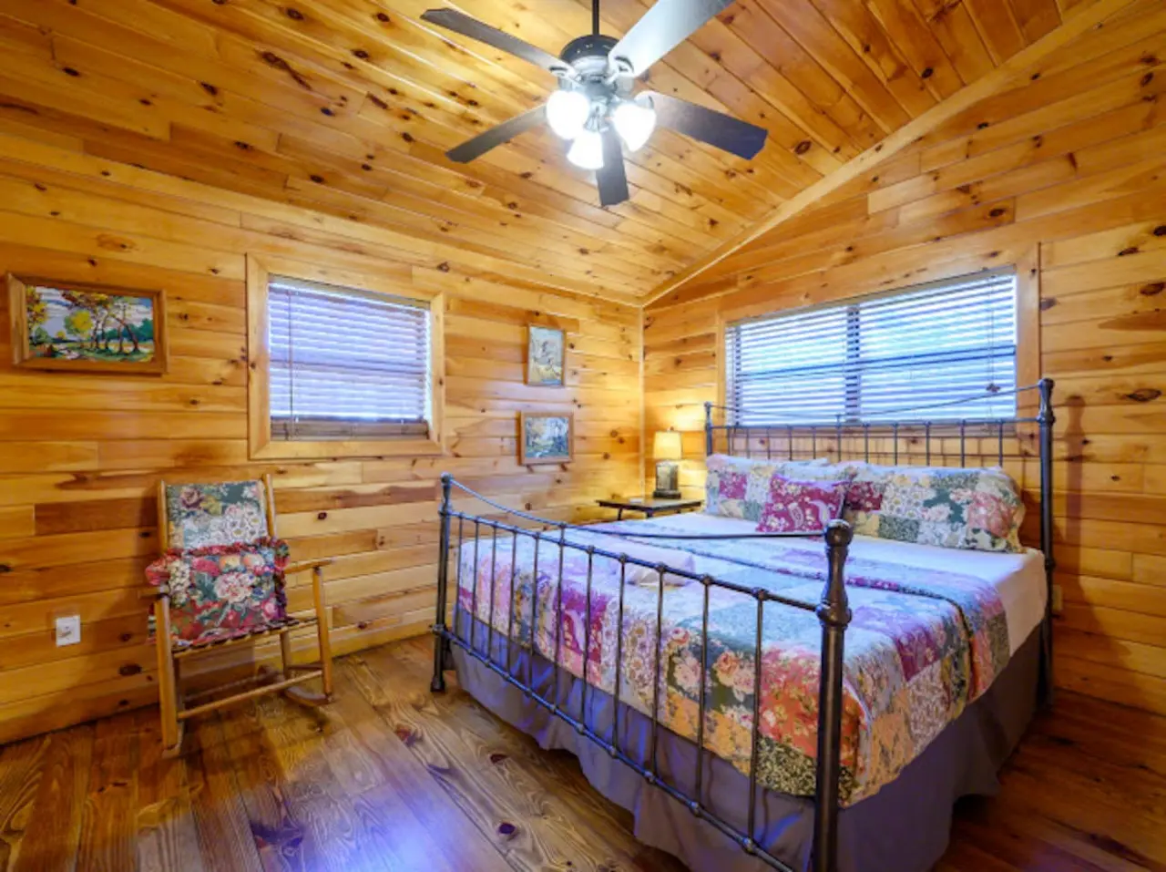 This cozy log cabin bedroom features a charming iron bed, wood-beamed ceilings, and plenty of natural light from the windows.