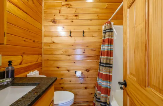 This cozy log cabin bathroom features warm wood walls, a granite countertop, and all the essentials for a comfortable stay.