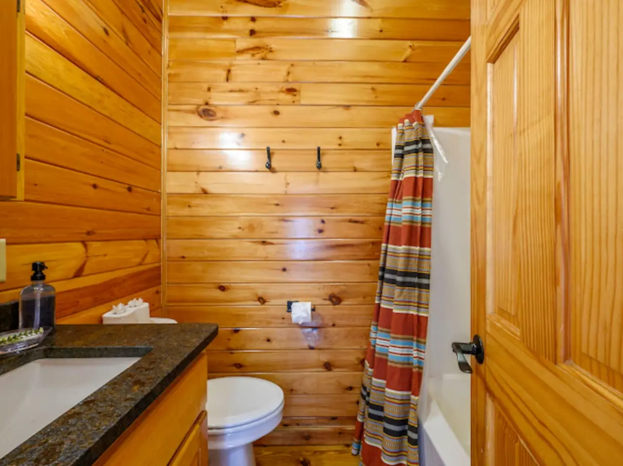 This cozy log cabin bathroom features warm wood walls, a granite countertop, and all the essentials for a comfortable stay.