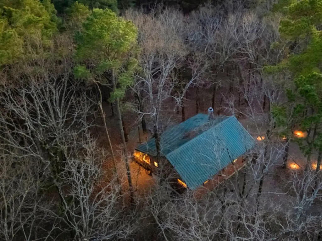 Cozy cabin nestled in the woods with warm lights glowing through the trees at dusk.