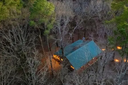 Cozy cabin nestled in the woods with warm lights glowing through the trees at dusk.