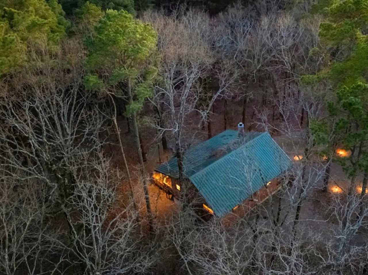 Cozy cabin nestled in the woods with warm lights glowing through the trees at dusk.