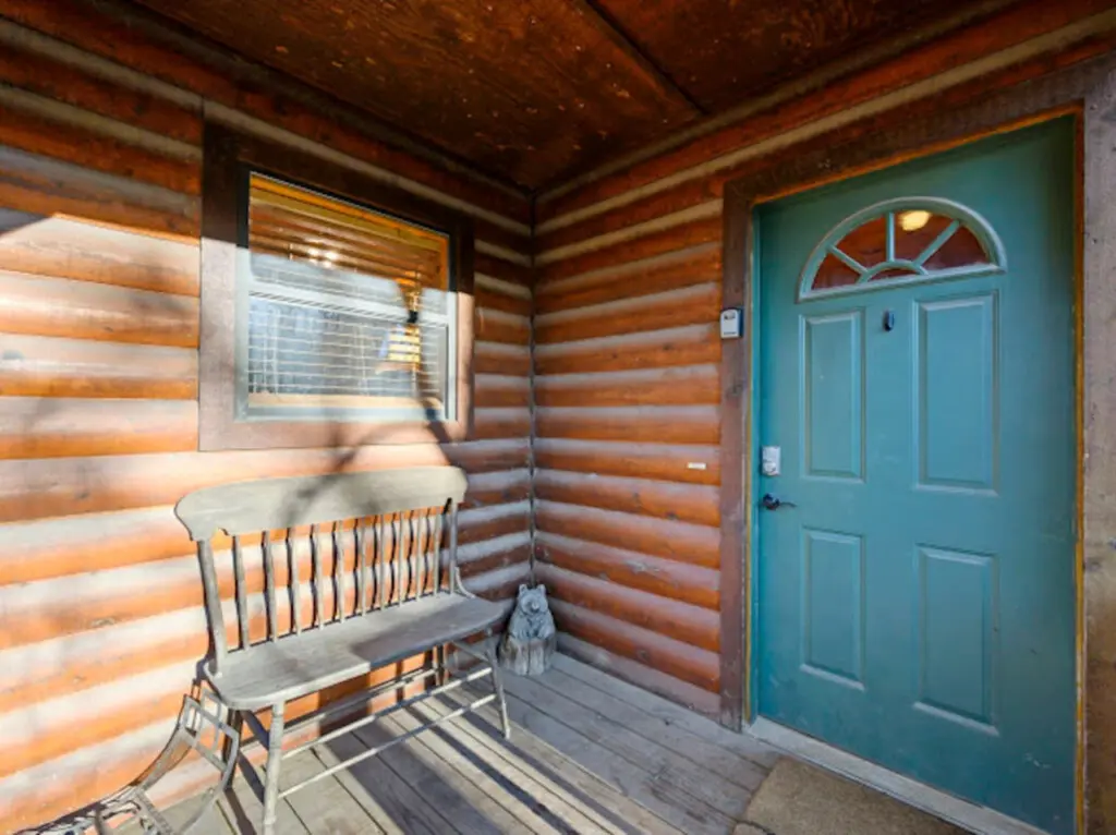Step inside this charming log cabin with its cozy front porch, rustic wooden beams, and inviting turquoise door.