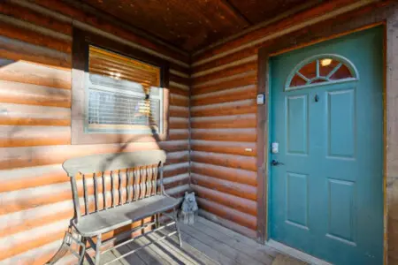 Step inside this charming log cabin with its cozy front porch, rustic wooden beams, and inviting turquoise door.