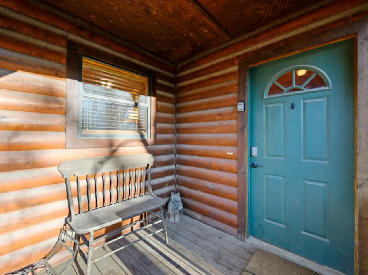 Step inside this charming log cabin with its cozy front porch, rustic wooden beams, and inviting turquoise door.
