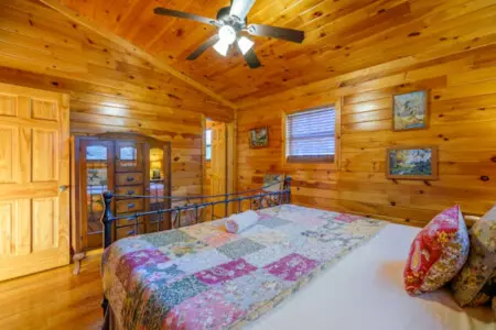 This cozy log cabin bedroom features warm wood throughout, a comfortable bed, and a ceiling fan to keep things cool.