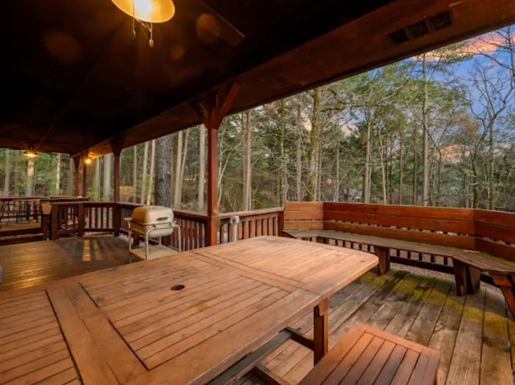 Spacious covered deck with cornhole, dining table, and stunning forest views perfect for relaxing outdoors.